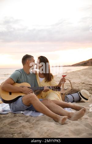 Lovely couple with guitar and picnic basket on beach at sunset Stock Photo