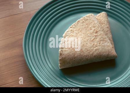 A folded wholegrain wrap on a green plate. Stock Photo