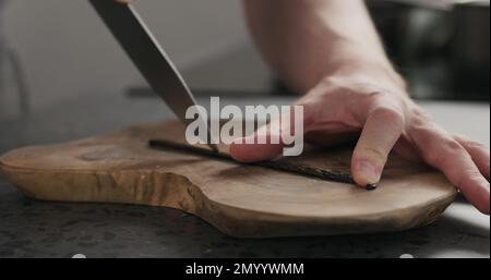 Man cut vanilla pod on olive wood board, wide photo Stock Photo