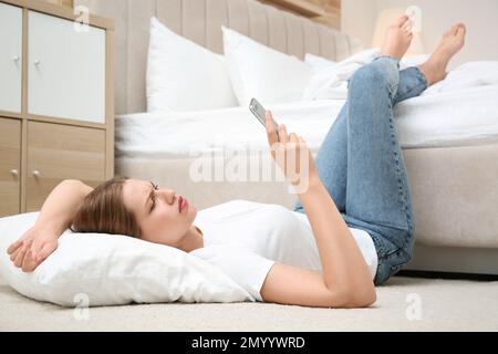 Lazy young woman with smartphone lying on floor at home Stock Photo