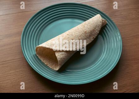 A folded wholegrain wrap on a green plate. Stock Photo