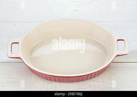 Red ceramic baking dish in wooden background. Empty oval baking dish for gratin. Stock Photo
