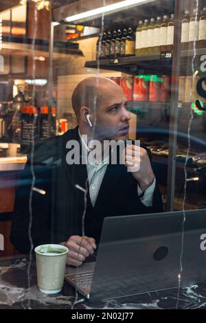 man young businessman entrepreneur caucasian,seriously enthusiast, bald in suit, sitting at a table, working laptop, talking via phone, remote job, in Stock Photo