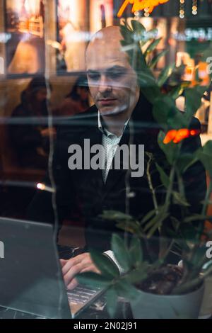 man young businessman entrepreneur caucasian,seriously enthusiast, bald in suit, sitting at a table, working laptop, talking via phone, remote job, in Stock Photo