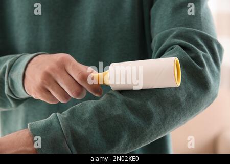 Man cleaning green sweatshirt with lint roller on light background, closeup Stock Photo