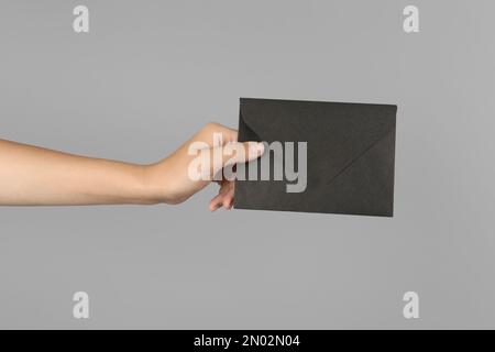 Woman holding black paper envelope on light grey background, closeup Stock Photo