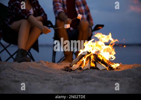 People roasting marshmallows over burning firewood on beach, closeup Stock Photo