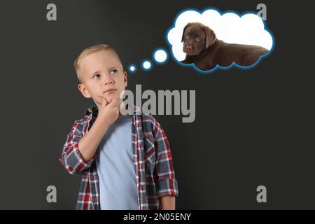 Little boy dreaming about cute puppy, dark background Stock Photo