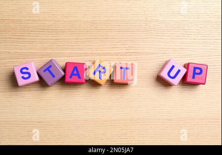 Words START UP made with color cubes on wooden background, flat lay Stock Photo
