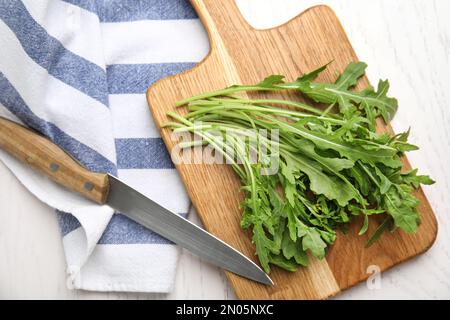 Fresh arugula, cutting board and knife on white wooden table, flat lay Stock Photo