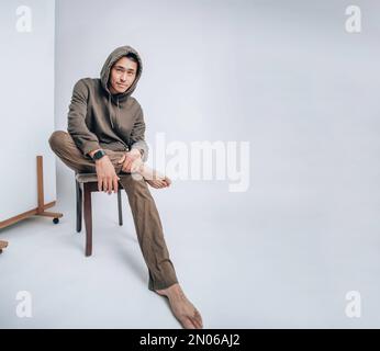 A young Asian man in a hoodie sitting on a white background Stock Photo