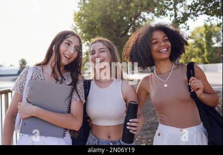 Group of teenagers of different nationalities and appearance have a fun together. Young and positive student girls in casual clothes with backpacks la Stock Photo