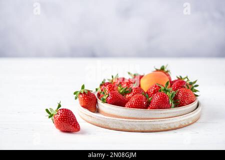 Fresh strawberries and apricot in two ceramic plates on a white wooden table and a gray background. Copy space, close-up. Stock Photo