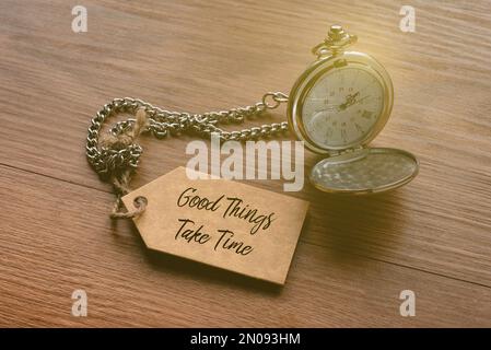 A pocket watch attached to a tag written with quotes Good Things Take Time. Stock Photo