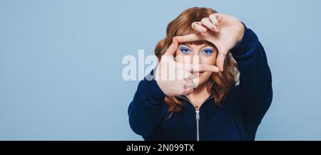 Woman looking at the camera while making a finger frame. Young woman with ginger hair isolated on a studio background. Stock Photo