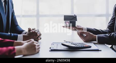 Real estate agent gives key to smiling clients. Happy couple signs papers and takes key to new home. Concept of young family making dream come true Stock Photo