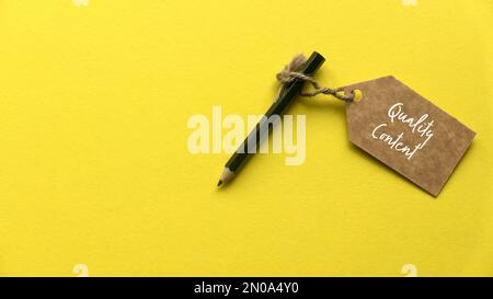 A pencil and brown tag written with quality content on yellow background. Stock Photo