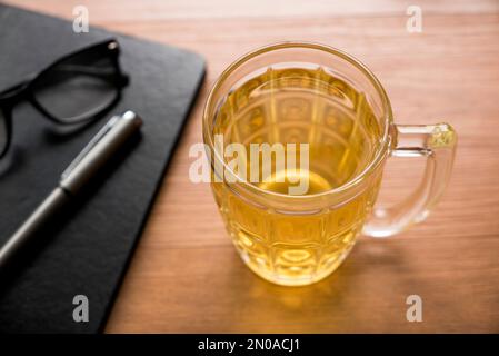 A glass of tea together with a glasses. pen and notebook on a wooden background. Stock Photo