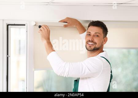 Handyman with screwdriver installing roller window blind indoors Stock Photo