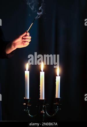 Hand igniting candles with match stick on the dark background. Condolence and mourning concept. Stock Photo