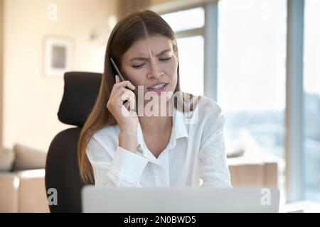 Puzzled worried freelance worker talking on mobile phone at workplace Stock Photo