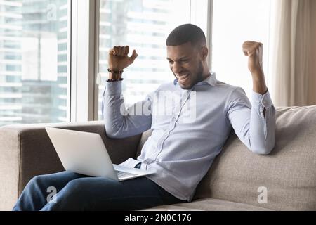 Happy excited millennial African laptop user man celebrating good news Stock Photo