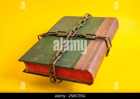 Old green bible with red pages tied with thick chains, floating on yellow background Stock Photo