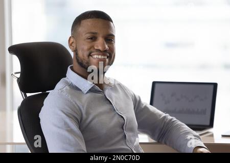 Cheerful confident young Black businessman sitting at office work table Stock Photo