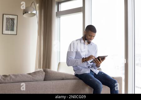 Happy handsome millennial African man touching tablet screen Stock Photo