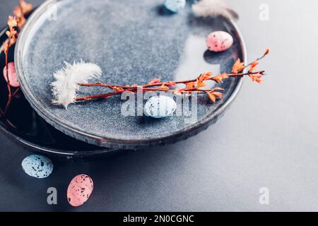 Easter pottery decoration. Close up of dishes with eggs, feathers and red spring branches. Lacquered ceramic plates on grey background. Holiday settin Stock Photo