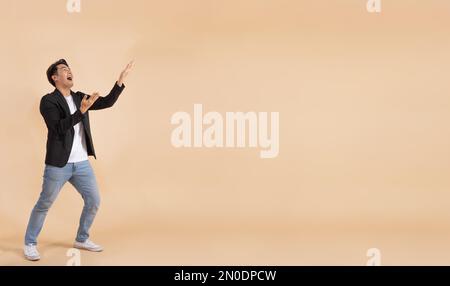 Happy smiling Asian businessman presenting empty copy space with two hands. Excited and amazed man in white shirt and suit on beige color background - used in ads promotion, advertising space, PR Stock Photo