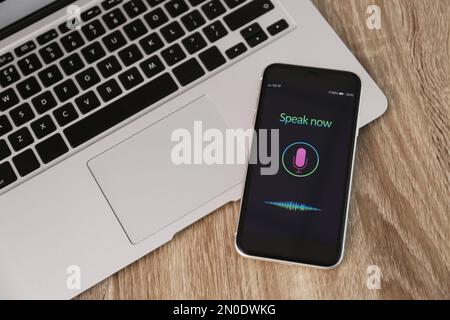 Smartphone with activated voice search app and laptop on wooden table Stock Photo