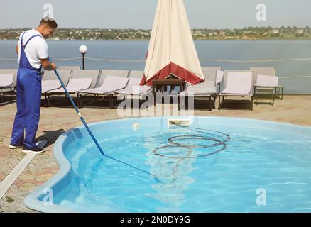 Worker cleaning outdoor swimming pool with underwater vacuum Stock Photo