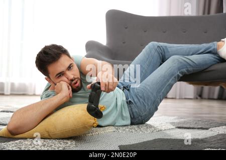 Lazy young man playing video game while lying on floor at home Stock Photo