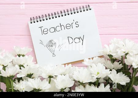 Beautiful flowers and notebook with words TEACHER'S DAY on pink wooden background, flat lay Stock Photo