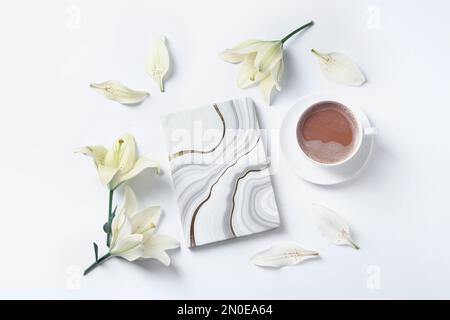 Beautiful lily flowers, cup of coffee and notebook on white background, flat lay Stock Photo