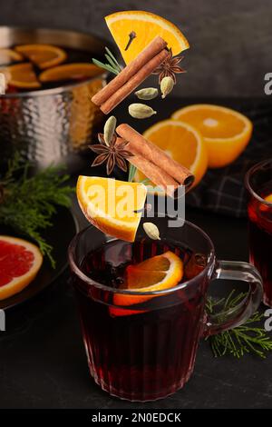 Cut orange and different spices falling into glass cup of mulled wine on table Stock Photo