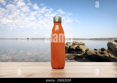 Thermo bottle on wooden table near sea under blue sky Stock Photo