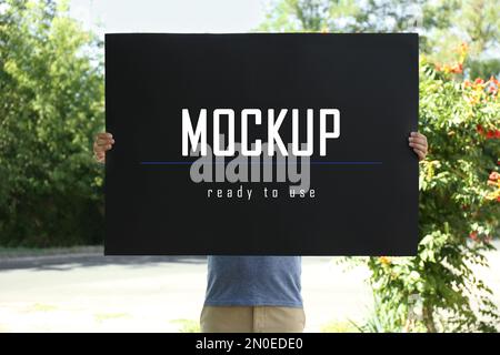 Man holding black poster with text Mockup Ready To Use outdoors Stock Photo