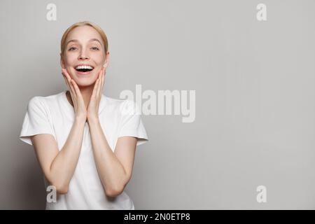 Happy smiling surprised blond woman posing against grey studio wall background Stock Photo