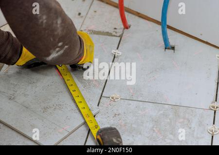 During preparation of laying floor tiles contractor measures ceramic tiles before they are cut into individual pieces Stock Photo