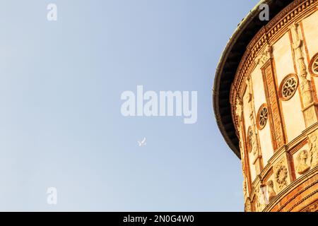 A red-yellow brick building with a light blue sky and a small airplane on the background of the sky Stock Photo