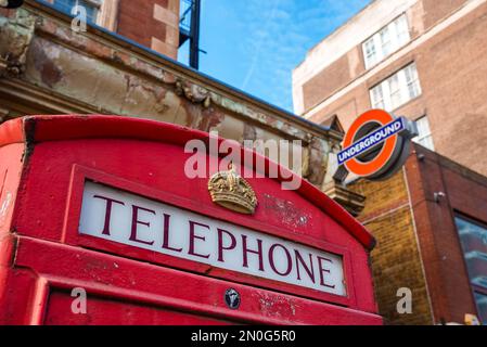 Typical London telephone booth on a rainy day and a beautiful subway station in the background. Stock Photo