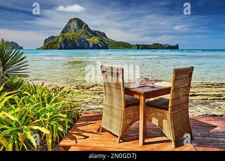 Outdoor terrace of the beach restaurant in front of sea with table and chairs, beautiful view to the Cadlao island, El Nido, Philippines Stock Photo