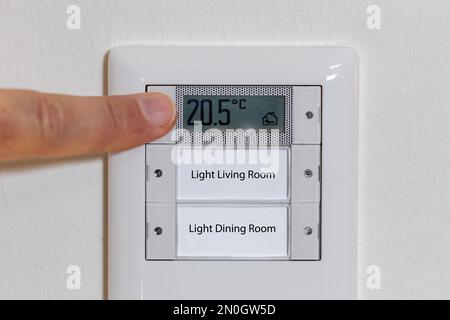 Man adjusting the temperature on a thermostat, reduce the temperature in the apartment in global energy crisis Stock Photo