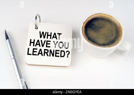 Business concept. On a white surface, a cup of coffee, a pen and a notepad with the inscription - what have you learned Stock Photo