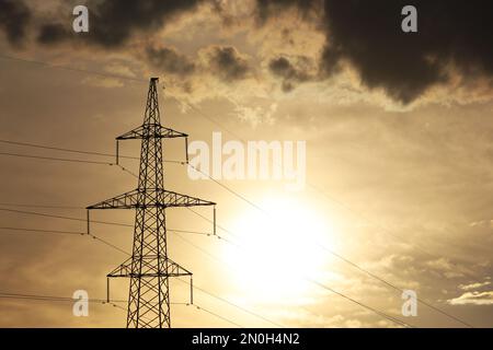 Silhouette of high voltage tower with electrical wires on background of sunset sky and dark clouds. Electricity transmission lines, power supply Stock Photo