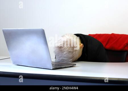 Girl with short dyed hair sleeping near the laptop at office table. Concept of overworked employee, tired after work, sleepless night Stock Photo