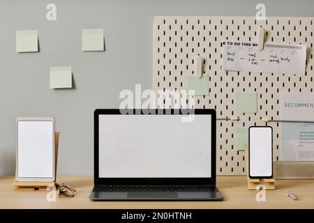 Front view mockup of three device screens, laptop tablet and phone at workplace Stock Photo