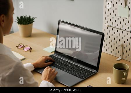 Closeup of young woman typing at laptop with white screen while working in office, copy space Stock Photo